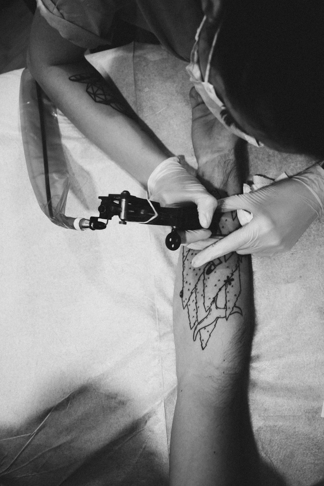 A tattoo artist skillfully designs a unique pattern on a client's arm in monochrome.